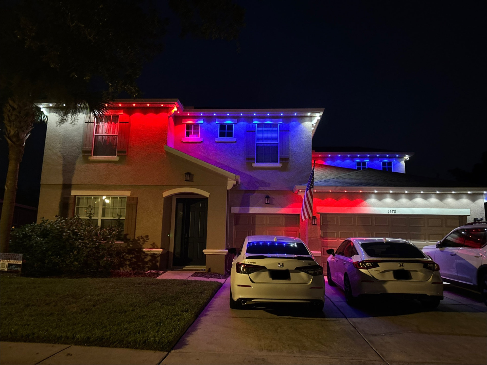 Two-story home with red, white, and blue patriotic permanent LED roofline lighting at night