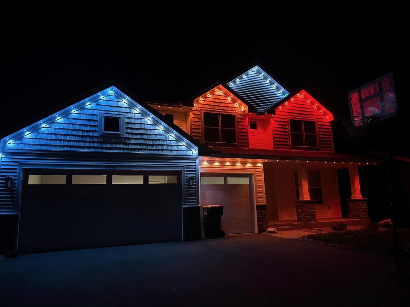 Two-story home with blue and red permanent LED roofline lighting at night